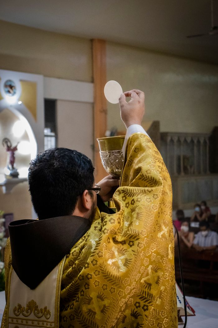 A priest in gold vestments holding a chalice and host during a Catholic mass.