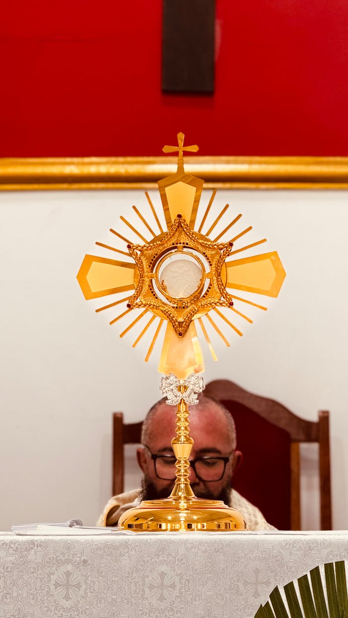 A golden monstrance displayed inside a church during a religious ceremony with a clergyman present.